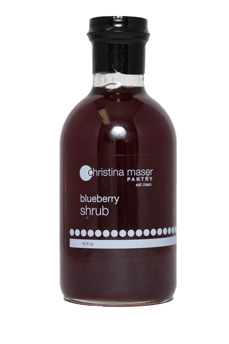 Blueberry Shrub or drinking vinegar in a wide glass bottle with a clear and white label. Made with organic sugar, apple cider vinegar, and local blueberries.