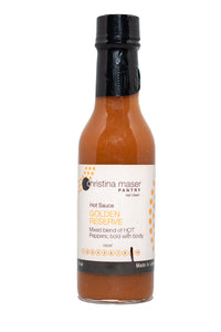 Golden Reserve hot sauce in glass bottle. Hot sauce is orange-red. Label is off white with orange accents. Lid is black.